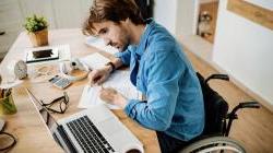 年轻的企业主坐在轮椅上，用笔记本电脑在桌子上处理文件